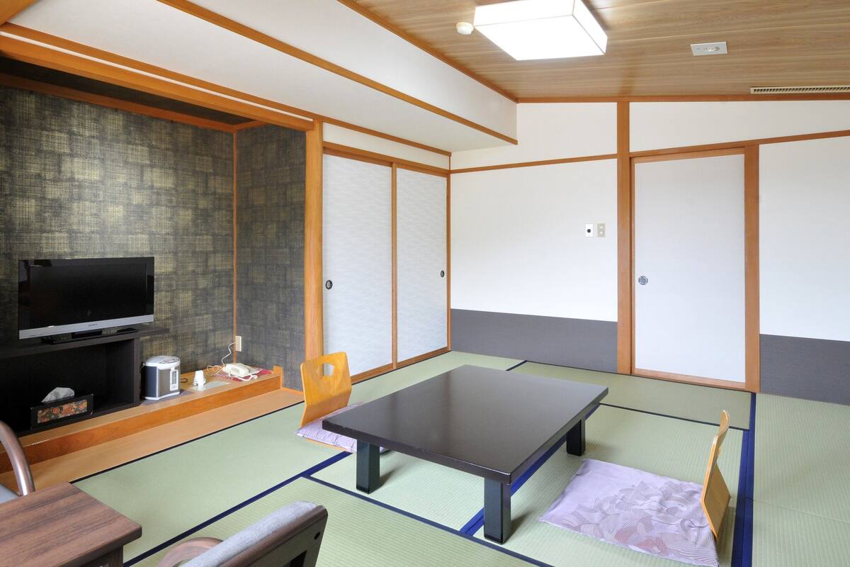 A traditional Japanese room with tatami flooring, a television, a table, and a sliding door.