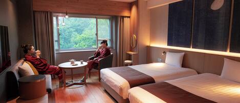 Habitación de hotel con dos camas, un sofá, una mesita y ventana con vista a árboles.