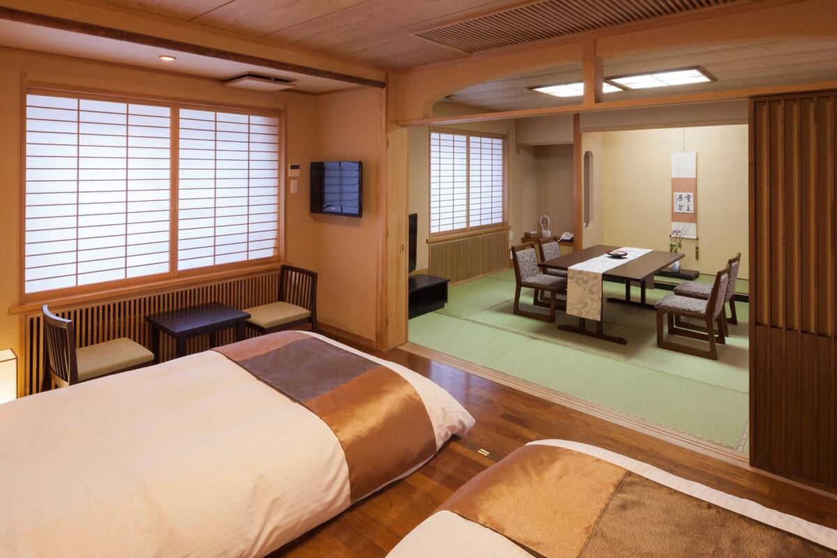 A traditional Japanese room with tatami flooring, a low table with chairs, a bed with a futon, and sliding doors.