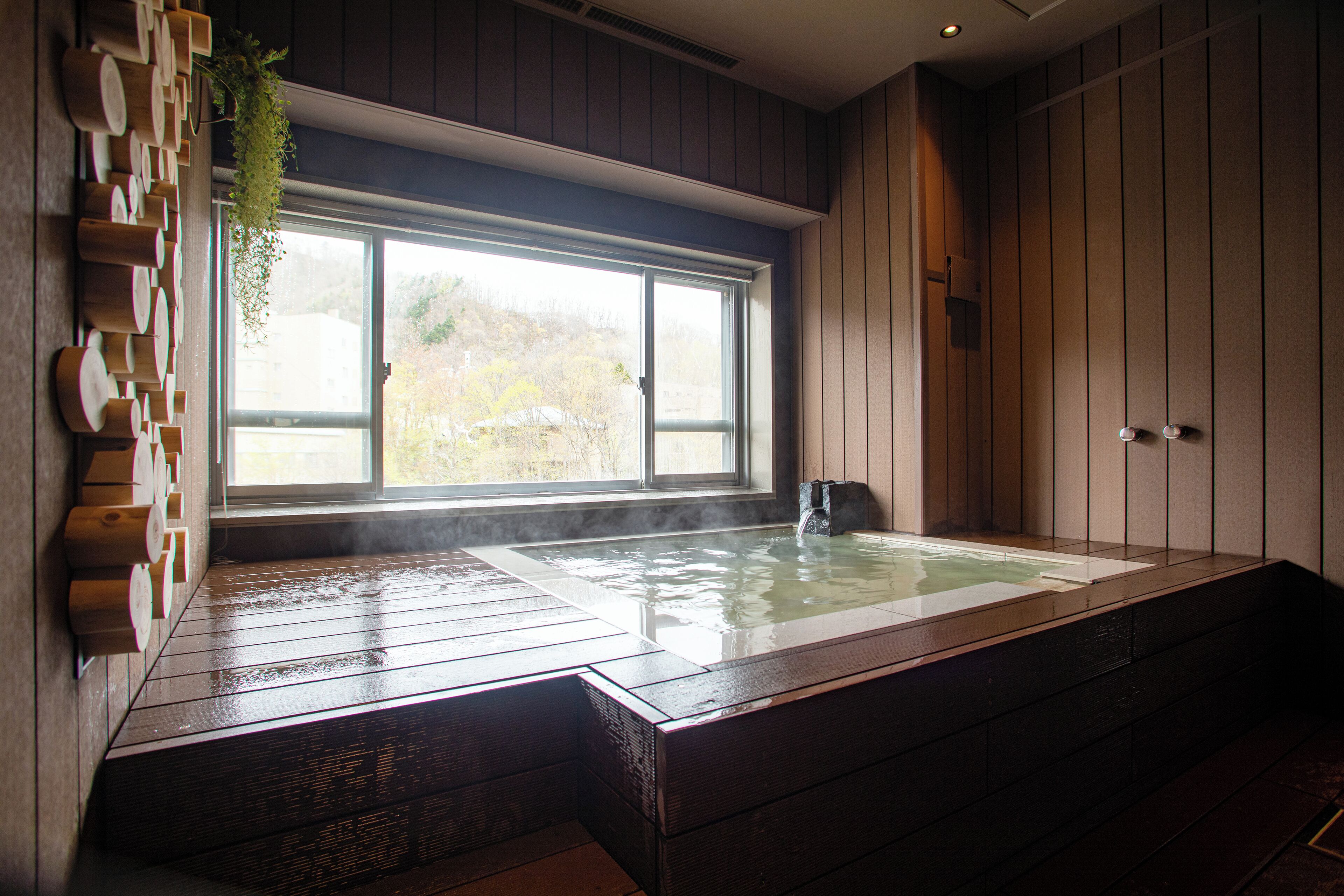 A hot tub with a view of a forest through a large window.