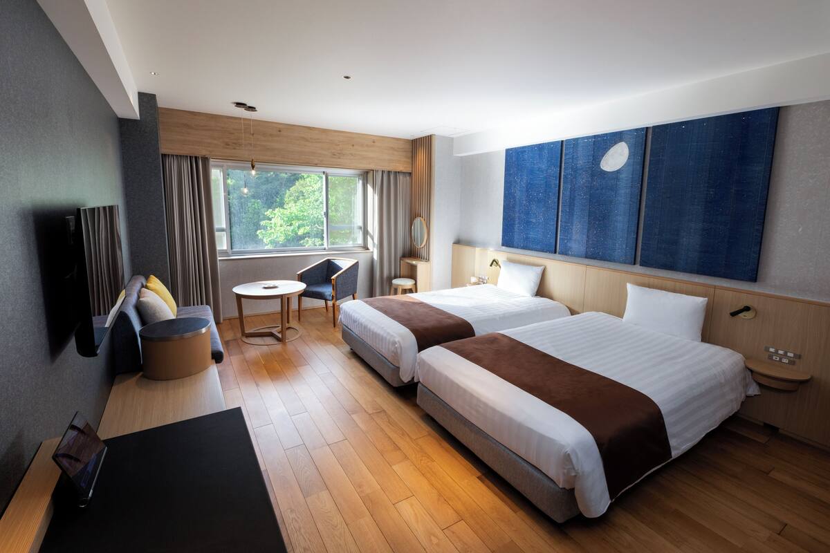 A hotel room with two beds, a desk, a chair, a TV, and a large window.
