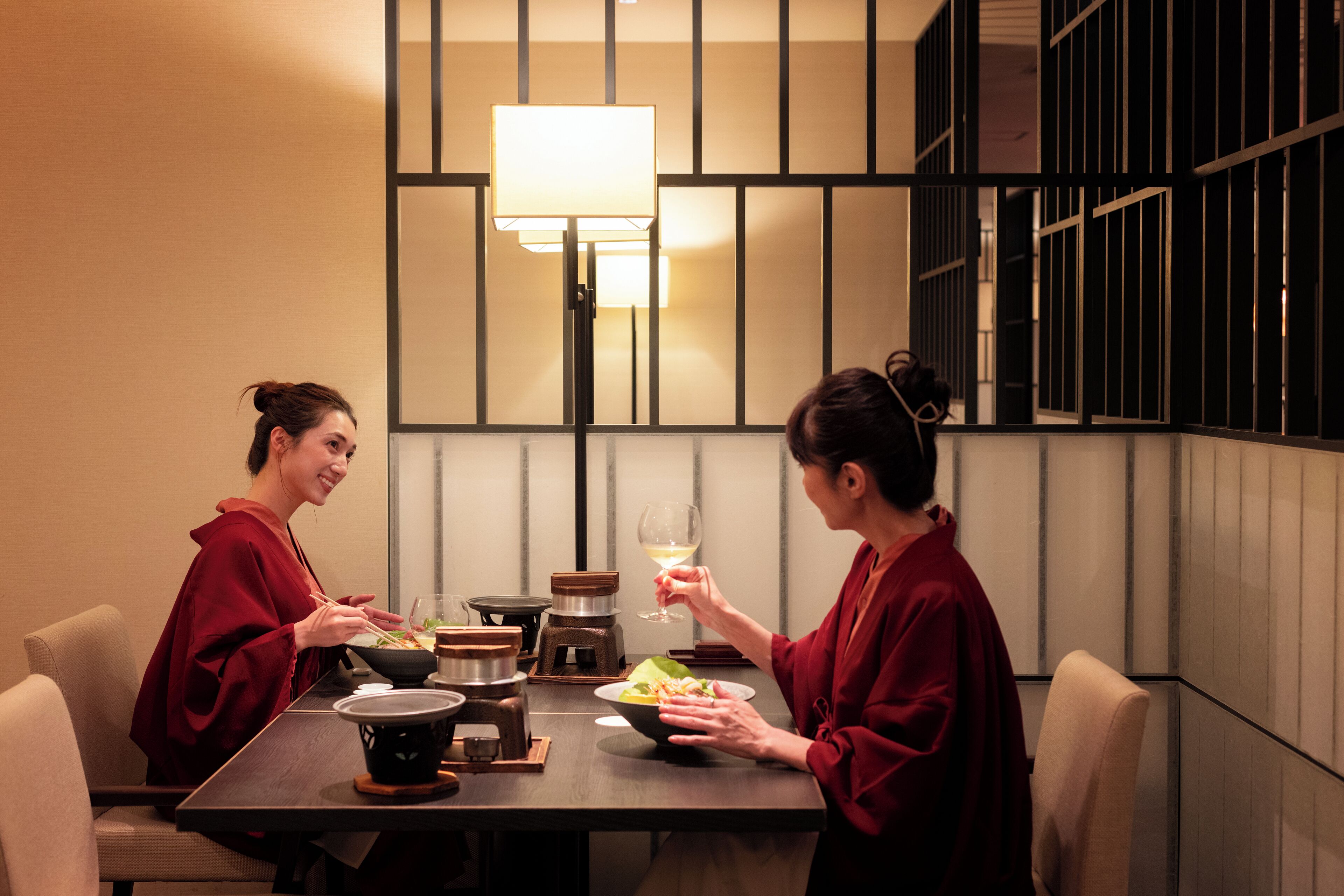 A dining table with two people seated, a bowl of food, and a wine glass.