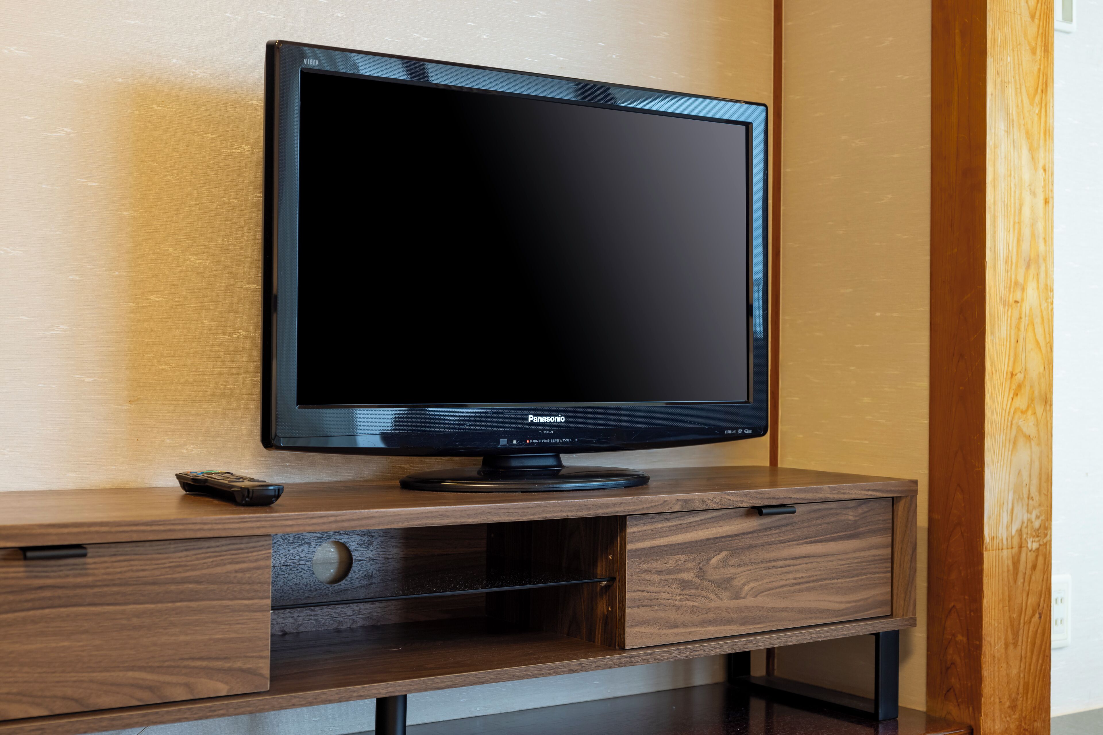 A flat-screen TV on a wooden TV stand with a remote control beside it.