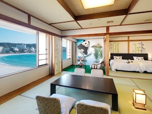 Une chambre dotée d’un grand lit, d’une table à manger, de chaises, d’une vue sur la plage et d’une fresque représentant des pandas.