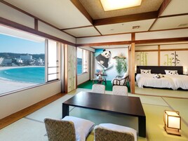Una habitación con una cama grande, una mesa de comedor, sillas, vista a la playa y un mural de pandas.