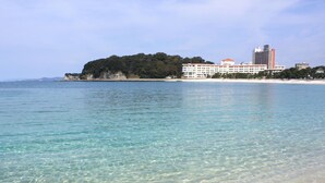 A coastal scene with clear turquoise waters, a sandy beach, and a large hotel building with multiple floors and a red roof. - Shiraraso Grand Hotel (Shirahama)