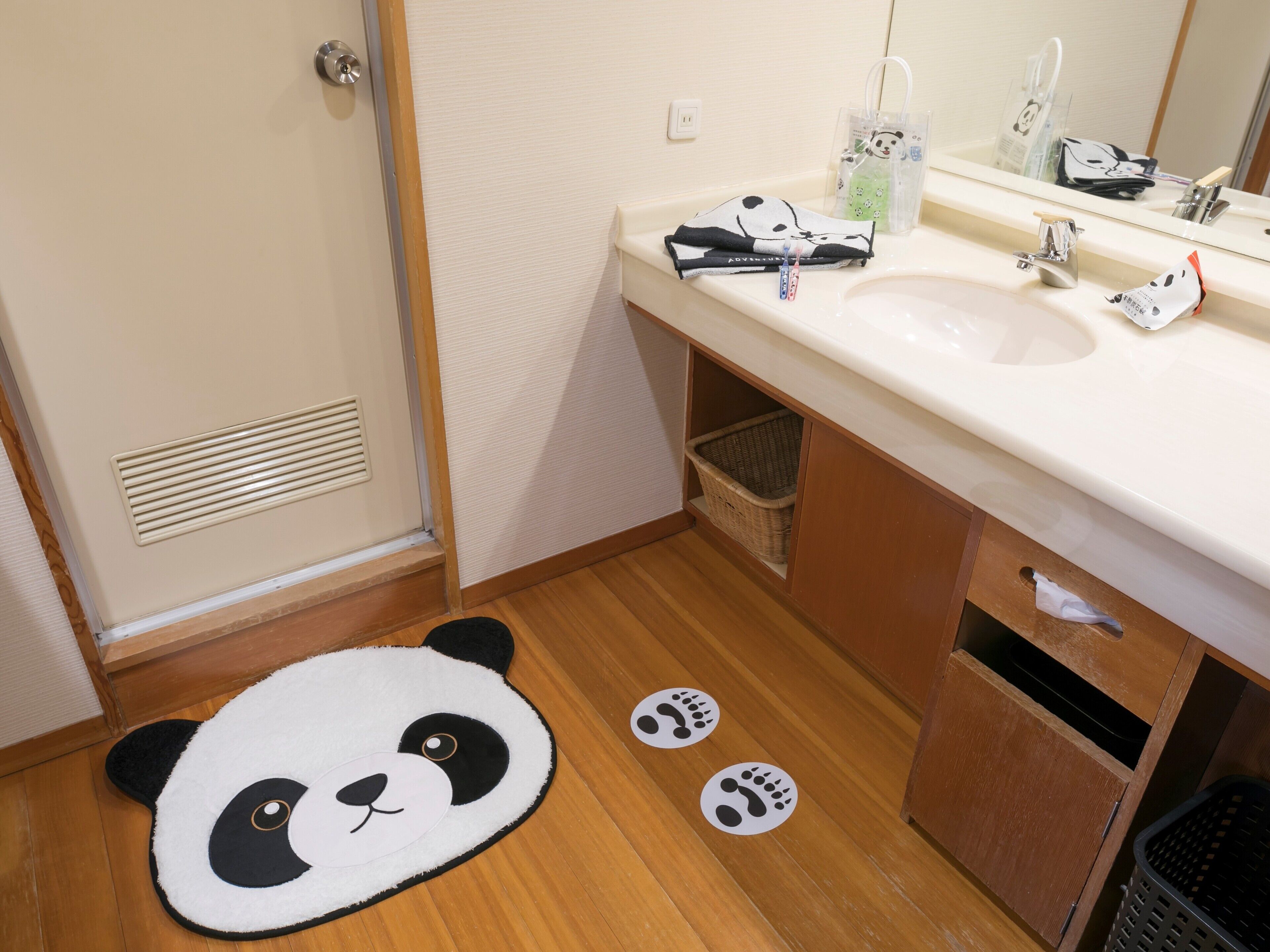 Un baño con un felpudo con temática de panda, un lavamanos, un espejo y una cesta debajo del mueble.