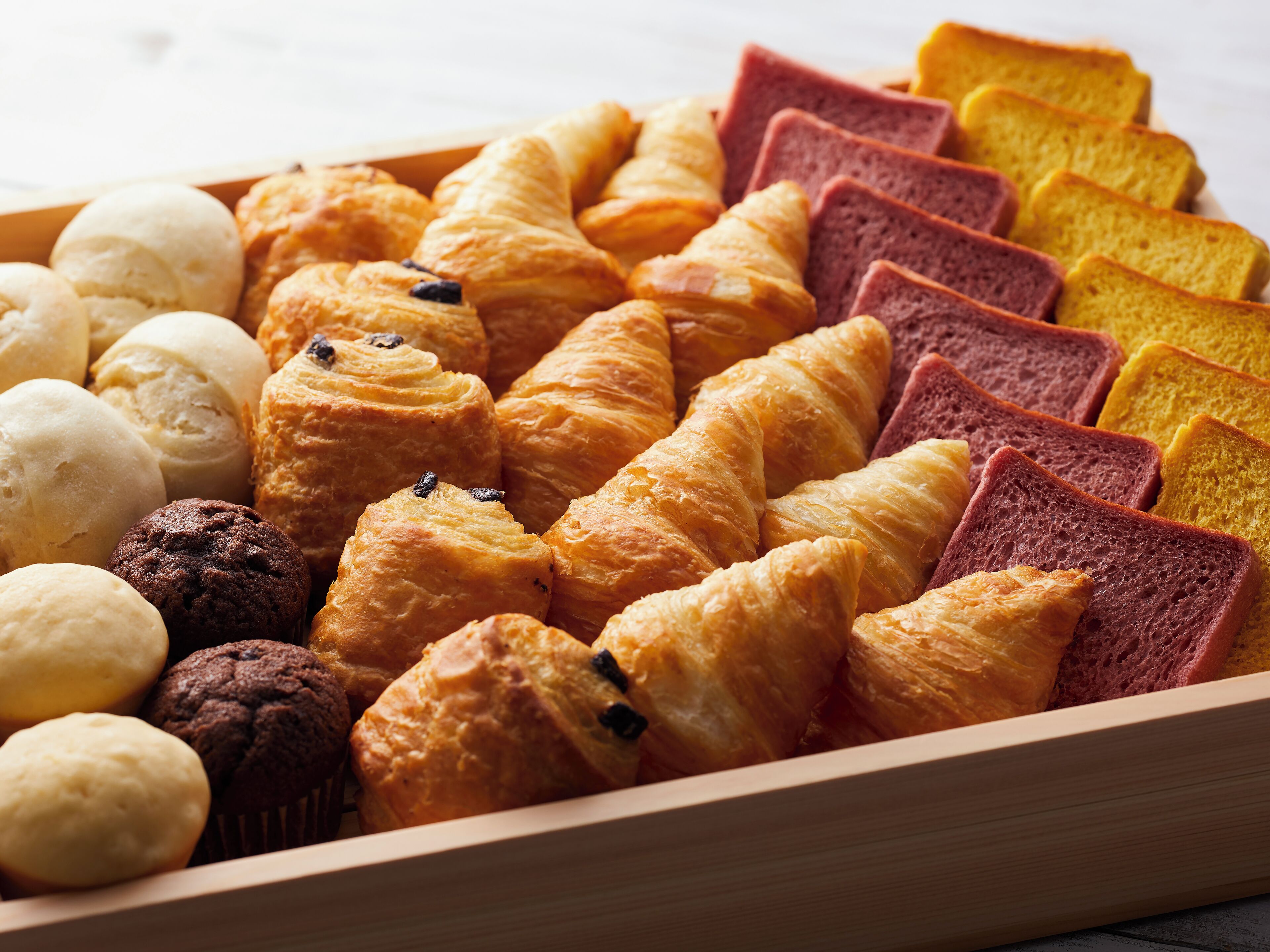 A variety of pastries including croissants, muffins, and bread slices in a wooden box.