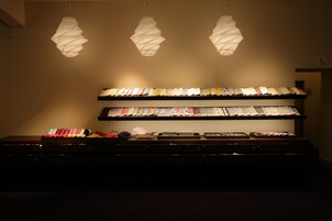 A display of neatly folded fabrics and a selection of quilts on shelves, illuminated by pendant lights.