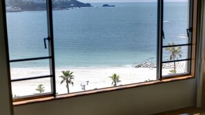 A room with a large window overlooking a beach with palm trees and a rocky shoreline. - Shiraraso Grand Hotel (Shirahama)