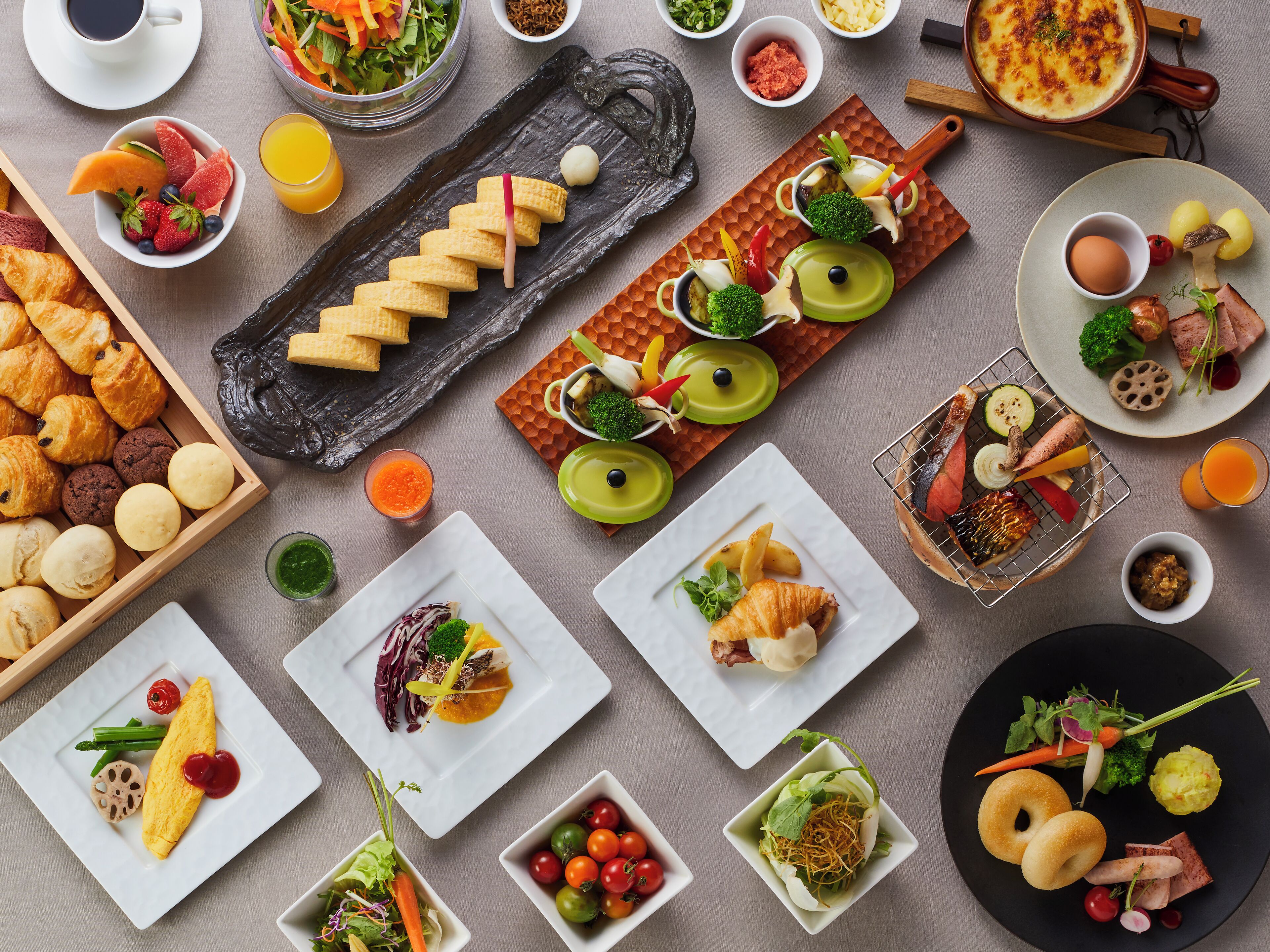 Diverse ontbijtartikelen, waaronder gebak, fruit, groenten en een warm gerecht, op een tafel.