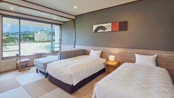 A hotel room with two beds, a small table, a chair, and a view of the beach.