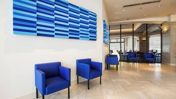 A modern lobby with blue chairs, a large abstract blue artwork, and a seating area with tables and chairs.