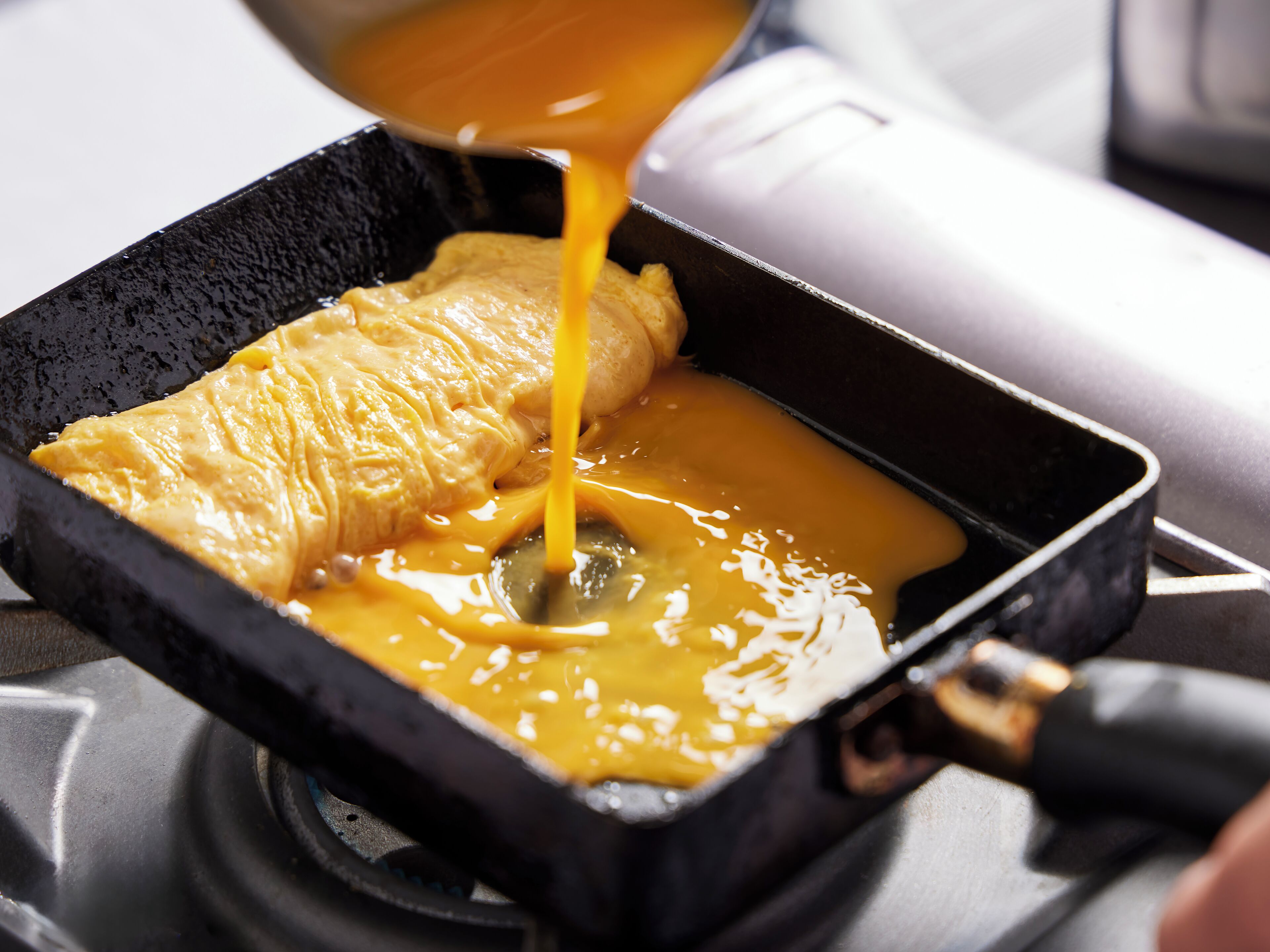 A pan with a golden-brown omelette and melted cheese being poured over it.