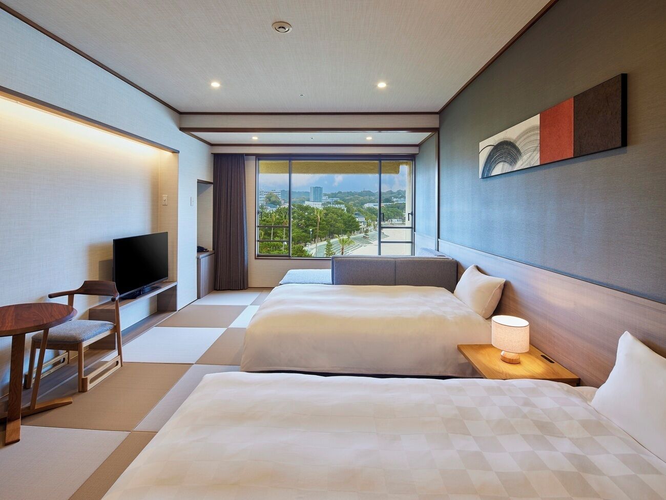 A hotel room with two beds, a TV, a desk, and a large window with a city view.