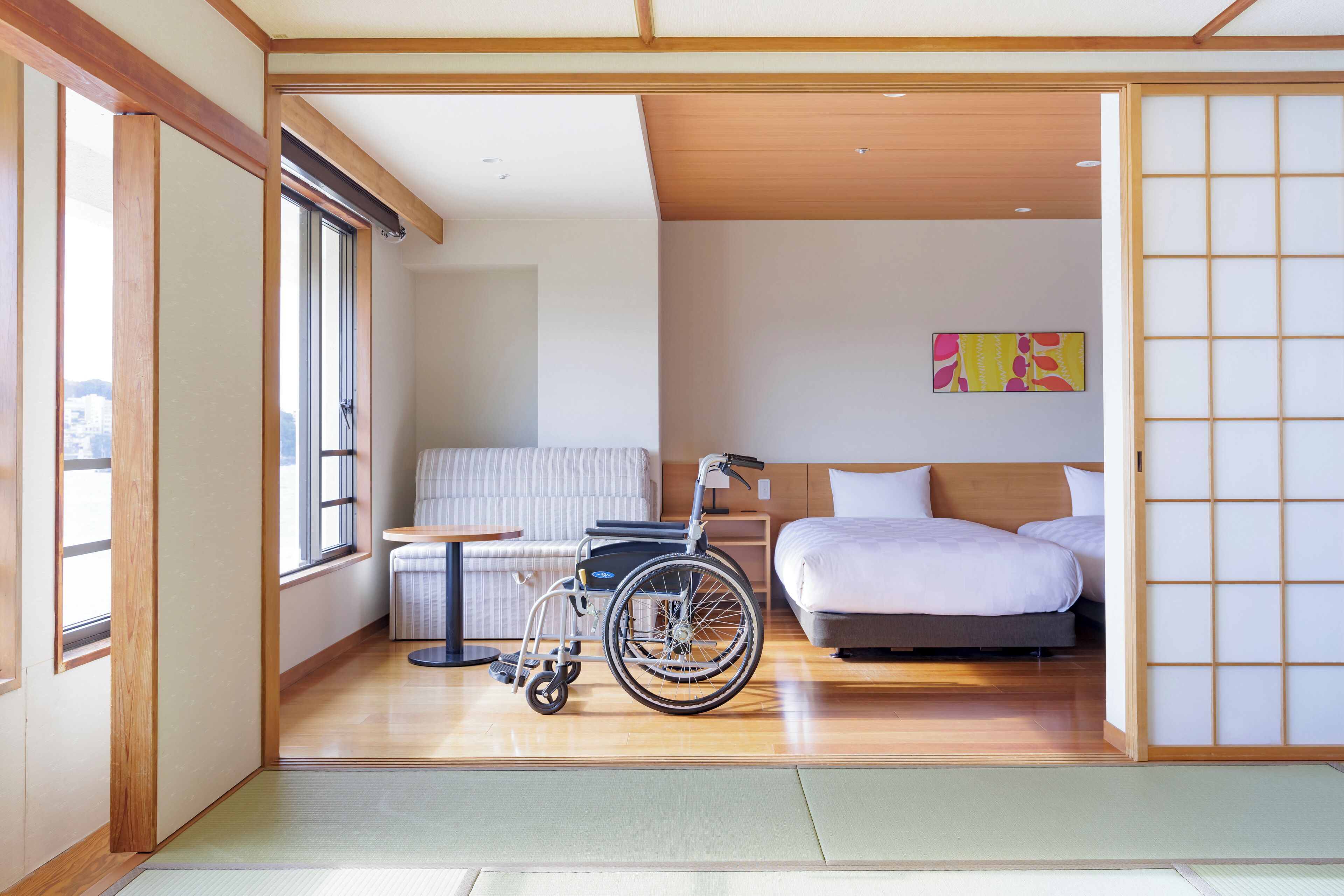 A room with a wheelchair, a bed, a sofa, and a tatami mat floor.