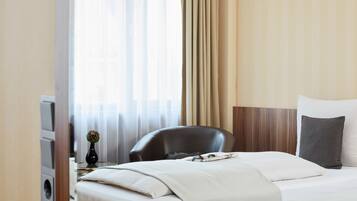 Quarto de hotel com cama, uma cadeira, uma mesinha com um vaso e uma televisão.