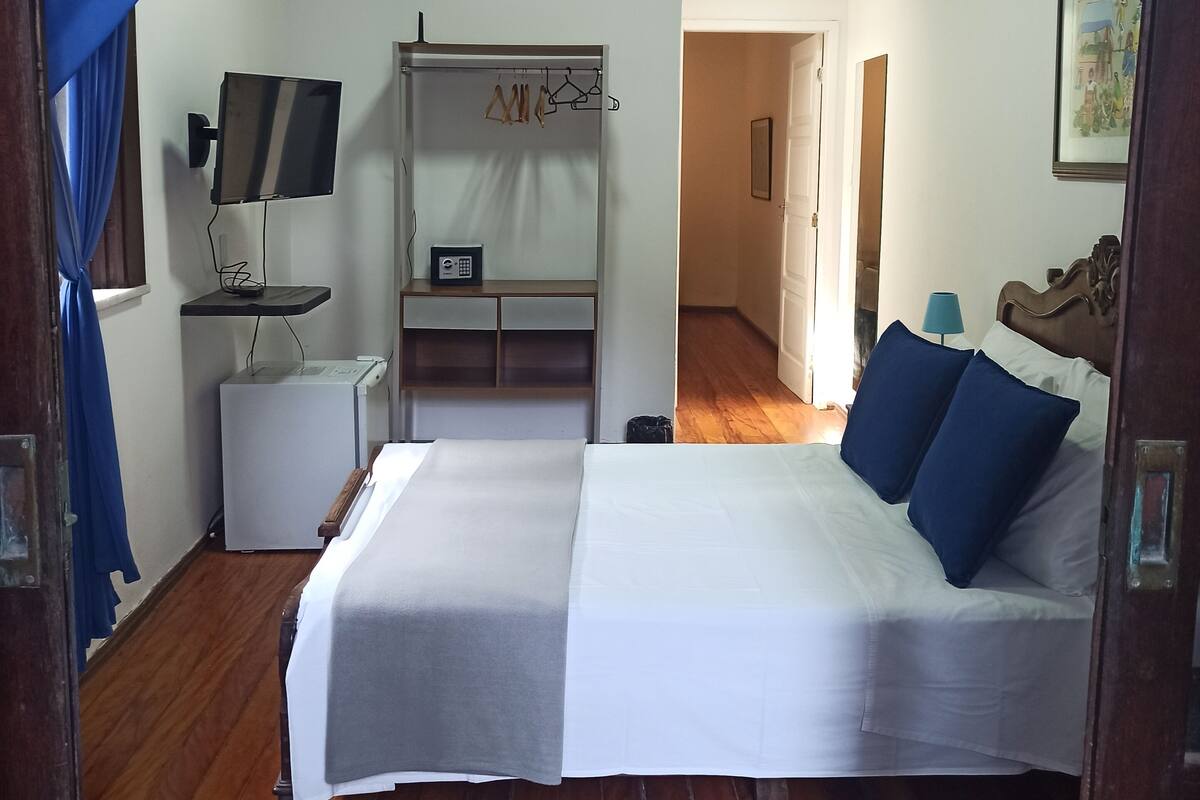 Ein Schlafzimmer mit Bett, Fernseher, Schreibtisch mit Computer und Kleiderschrank.