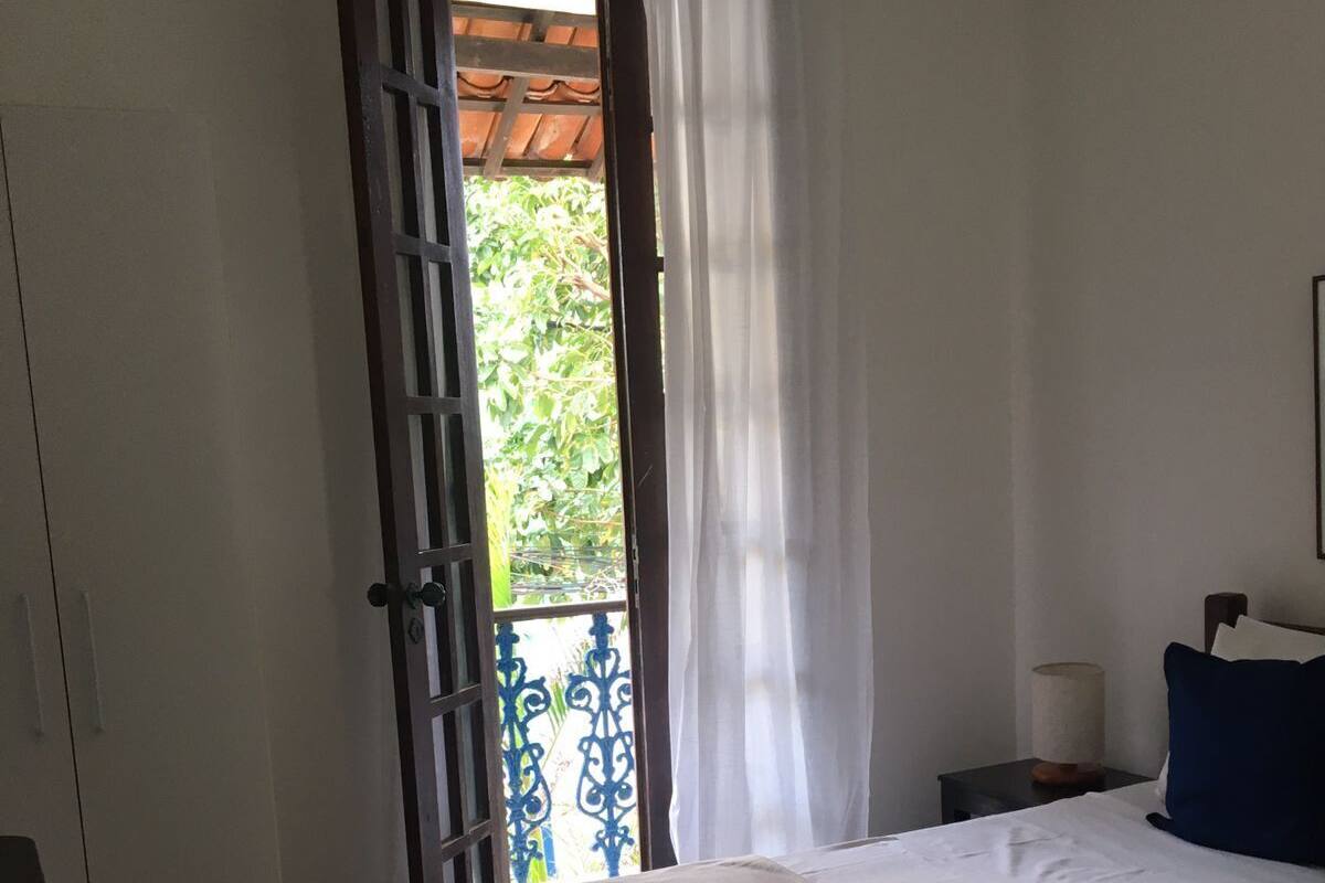 Ein Zimmer mit einem Bett, einem kleinen Tisch, einem Nachttisch, einem Heizkörper und einem Fenster mit Blick auf Grünflächen.