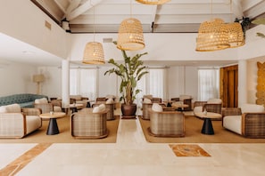 A spacious lobby with wicker furniture, a central potted plant, and hanging wicker lamps.