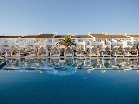 A hotel with a pool, white buildings, and a palm tree.