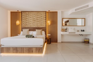 A modern hotel room with a wooden headboard, a large bed, bedside lamps, a bathroom with a mirror, sink, and toiletries.