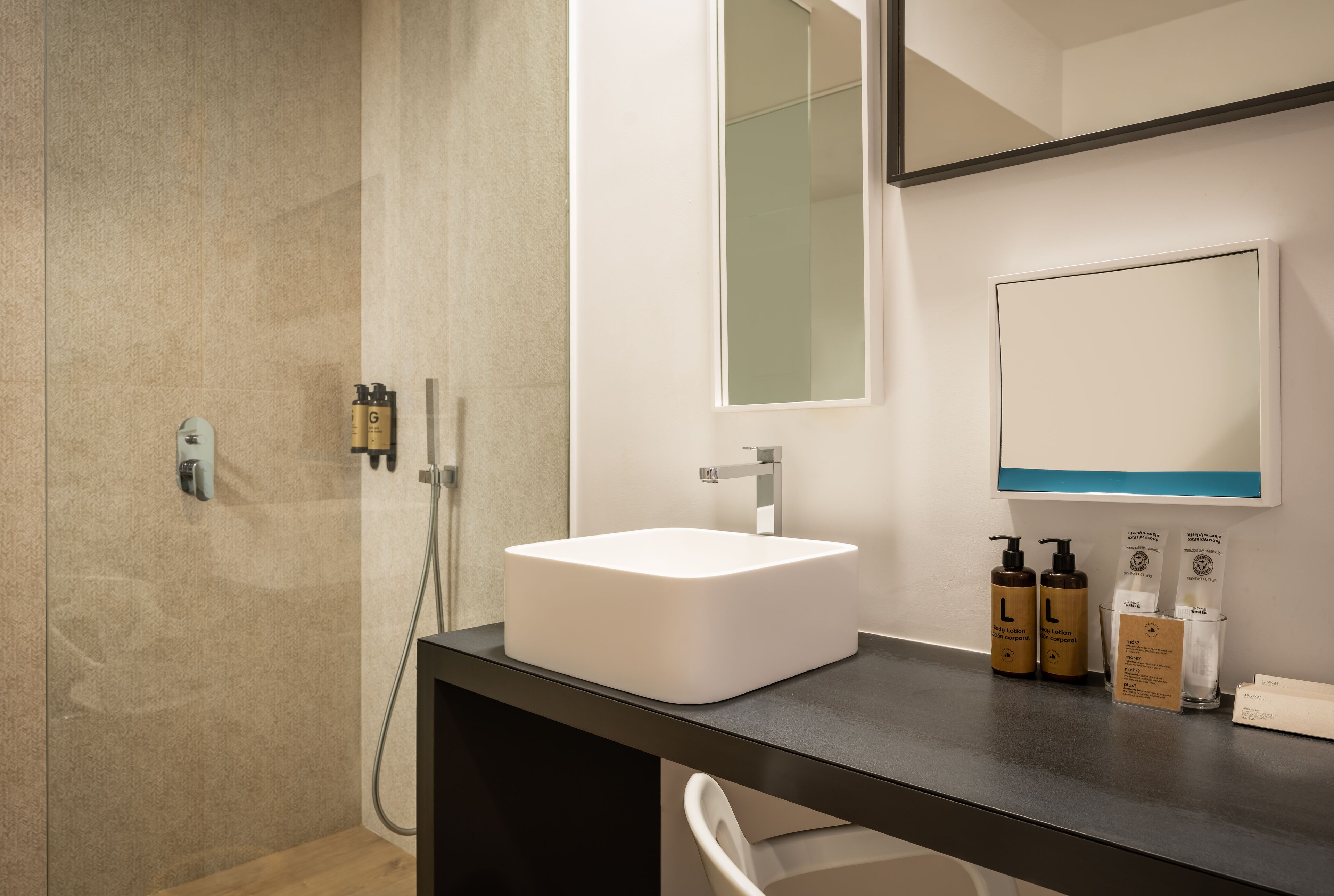 Un baño moderno con un lavabo blanco, un espejo grande y una zona de ducha.