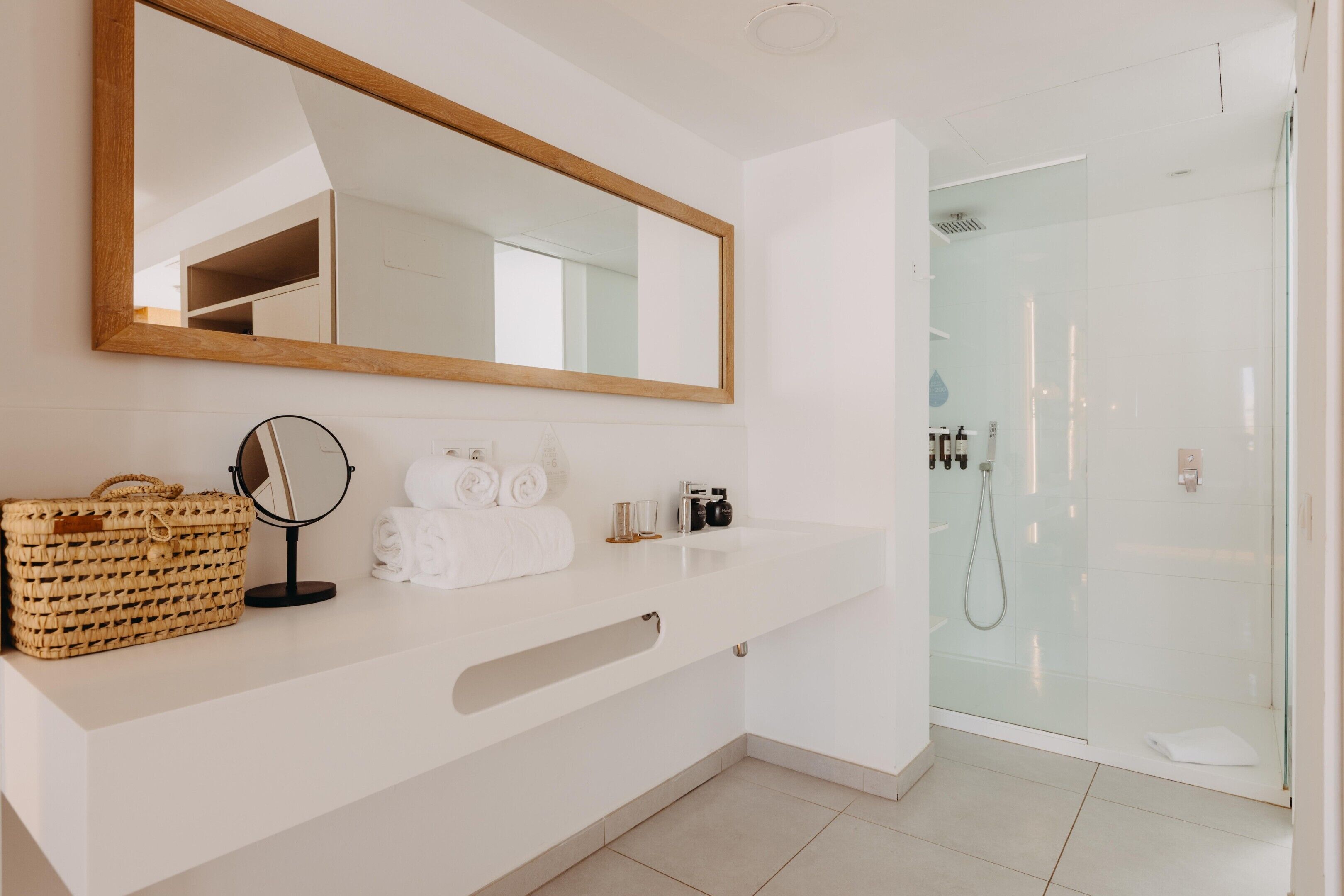Une salle de bain moderne avec un grand miroir, un meuble-lavabo avec un panier, des serviettes et des articles de toilette.