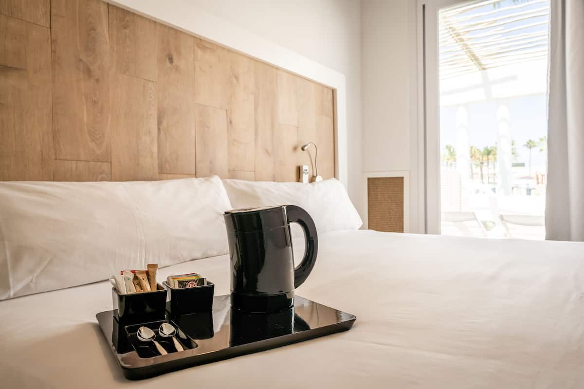 A hotel room with a wooden headboard, a tray with a coffee maker, cups, and utensils on the bed.