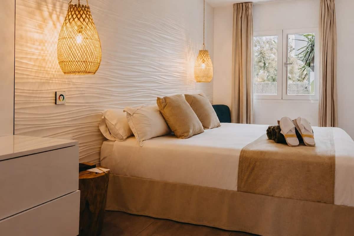 A neatly made bed with pillows, a bedside table, and a hanging light fixture.