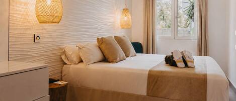 A neatly made bed with pillows, a bedside table, and a hanging light fixture.