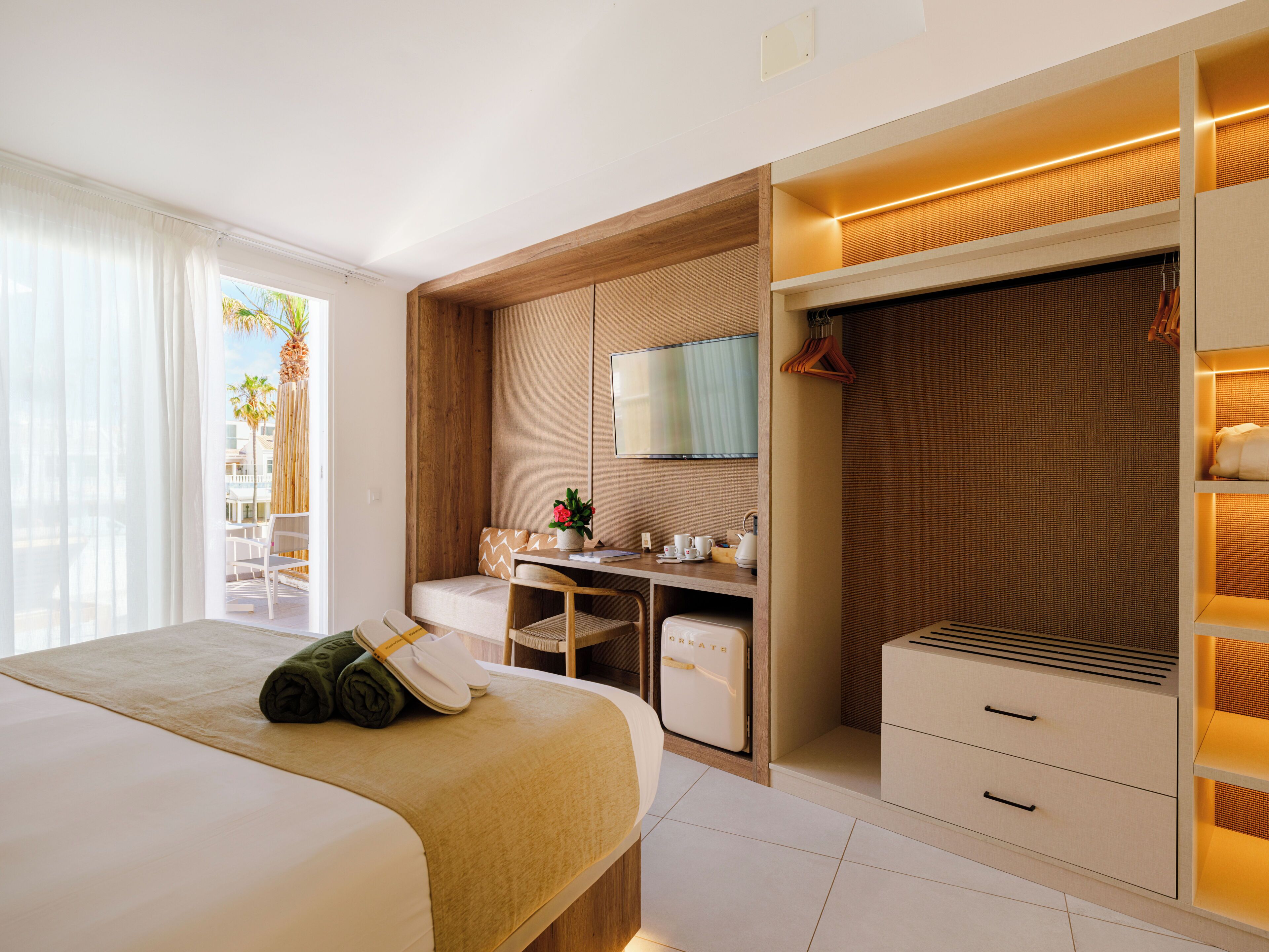 A hotel room with a bed, a desk, a chair, a wardrobe, and a view of the outdoors.