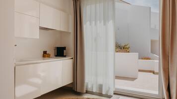 Cocina moderna con armarios blancos, cafetera y puerta corrediza de vidrio que da a un espacio exterior.