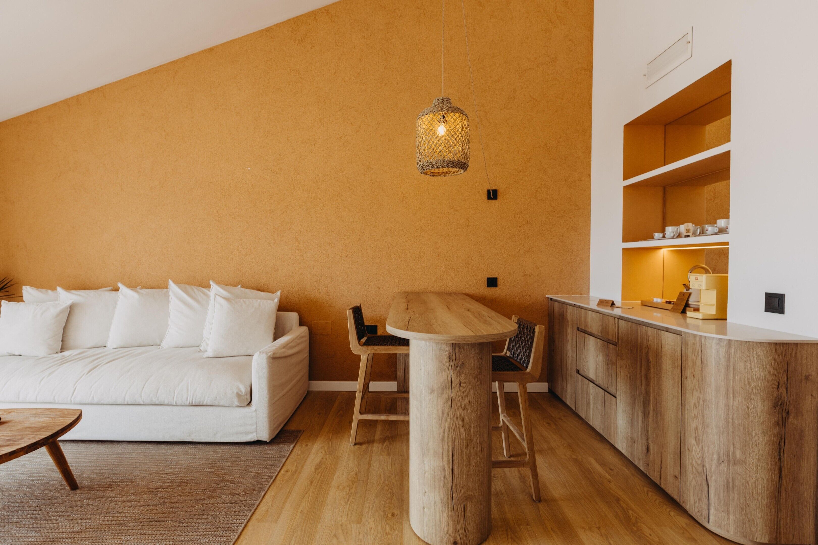 Un salon moderne avec une table à manger en bois, un canapé et un coin cuisine doté de meubles en bois et d’un luminaire suspendu.