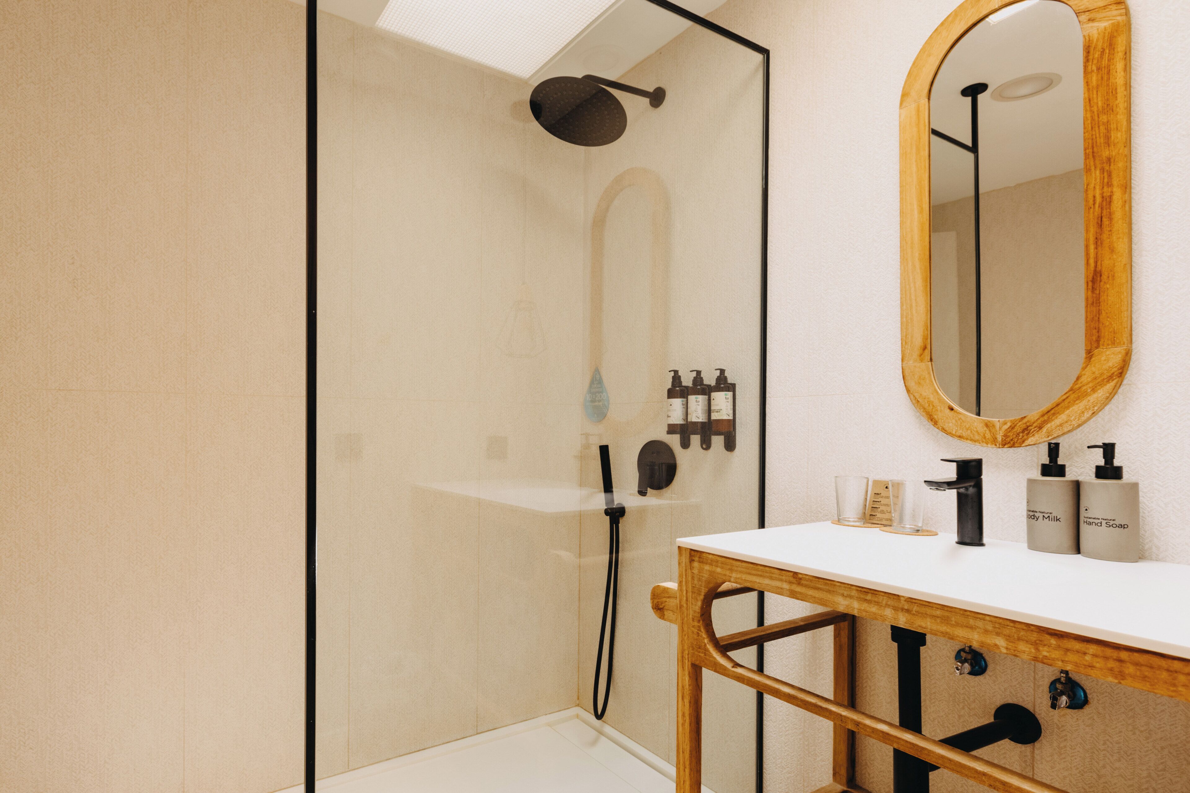 A modern bathroom with a glass-enclosed shower, a wooden vanity with a mirror, and toiletries on the counter.