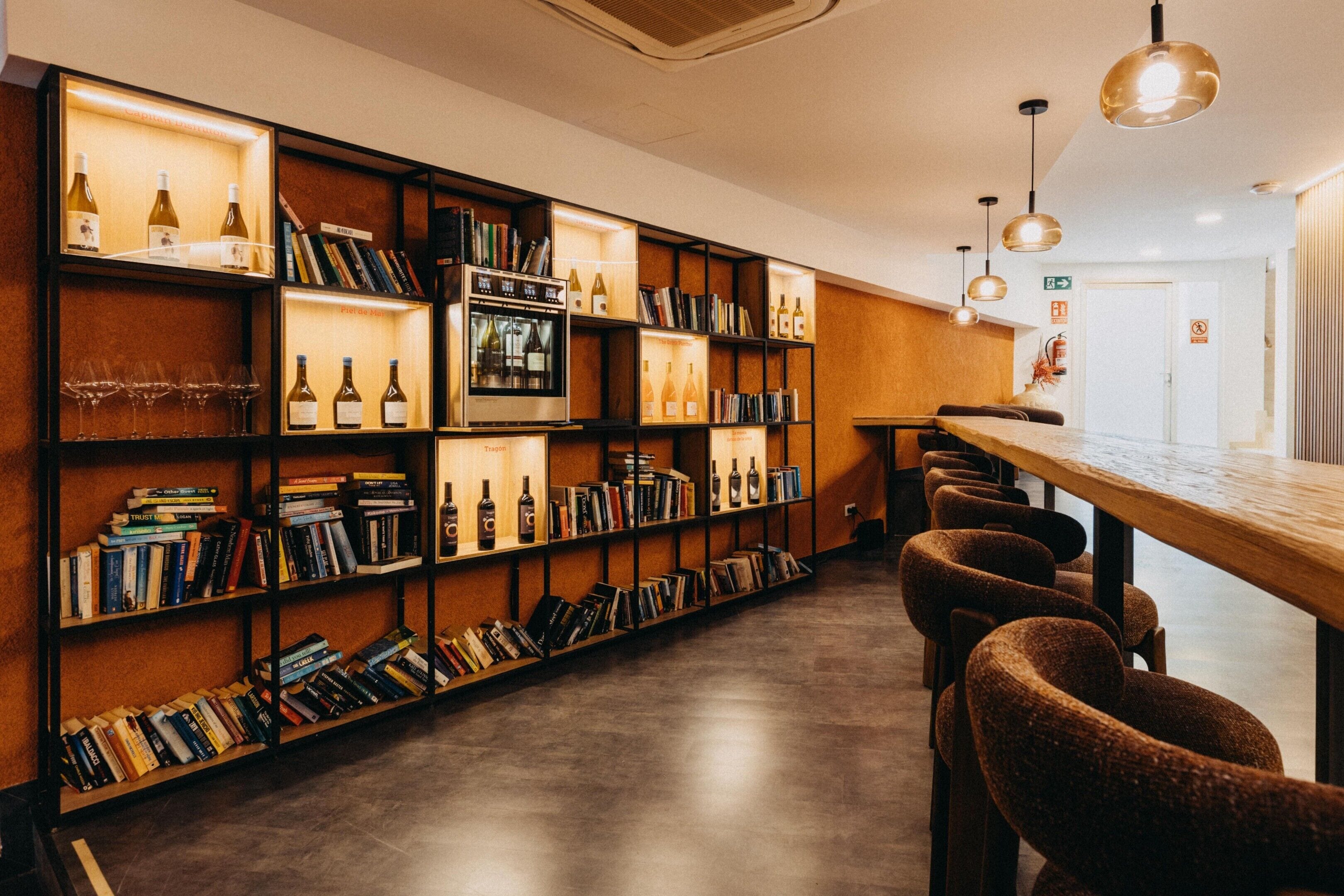 A library with bookshelves, wine bottles, and a long table with chairs.