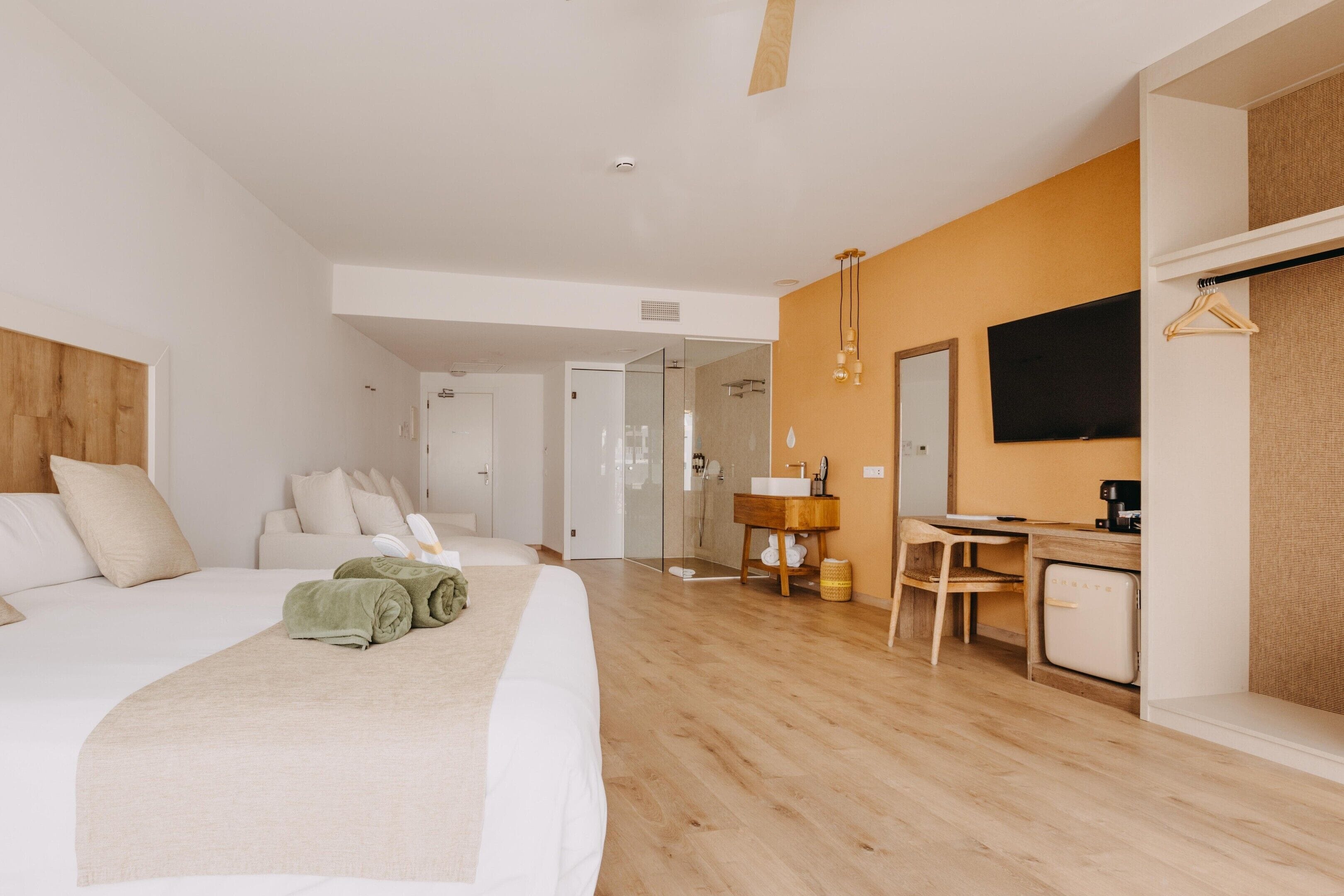 A modern hotel room with a large bed, a desk with a chair, a television, and a wardrobe.