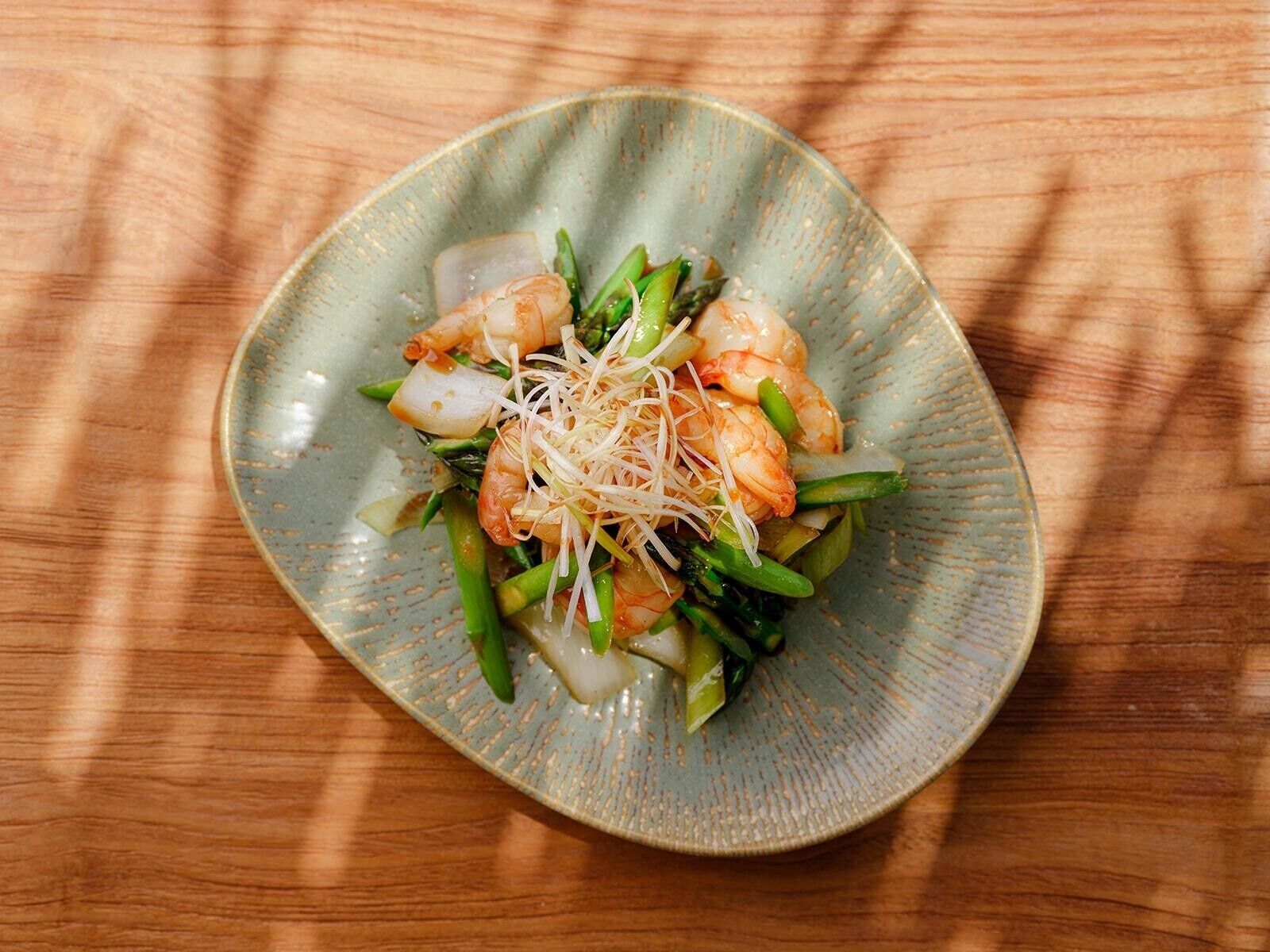 A plate of food with shrimp, green vegetables, and white noodles on a ceramic plate.
