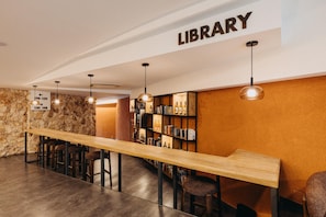 A library with a long wooden table, bookshelves, and hanging pendant lights.