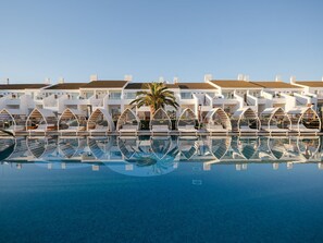 Ein Pool mit Liegestühlen und einer Palme, umgeben von weißen Gebäuden mit Balkonen.