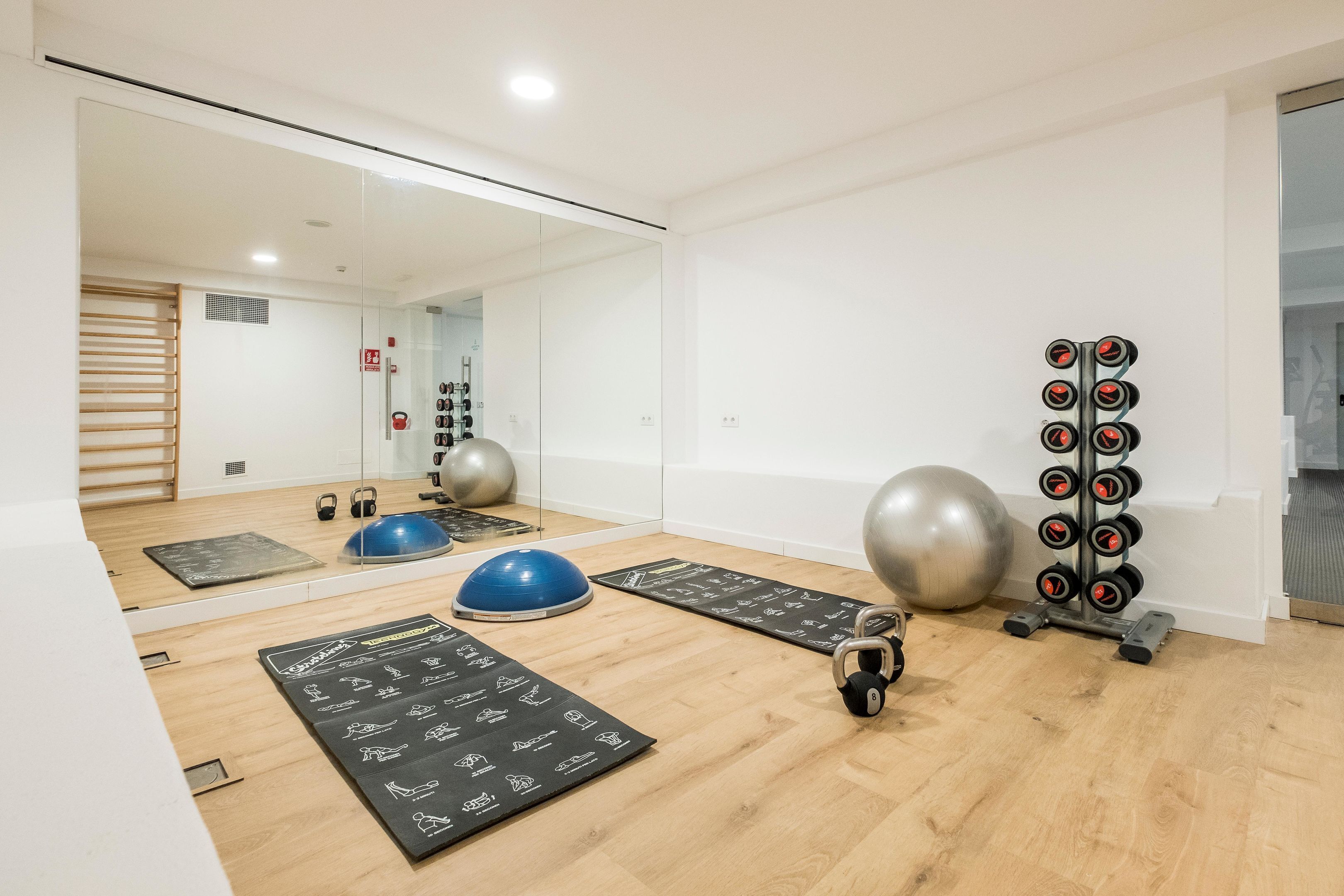 A gym with exercise equipment, a mirror, and wooden flooring.