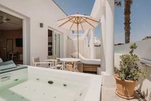 A modern outdoor area with a hot tub, white lounge chairs, a table, and a potted plant.