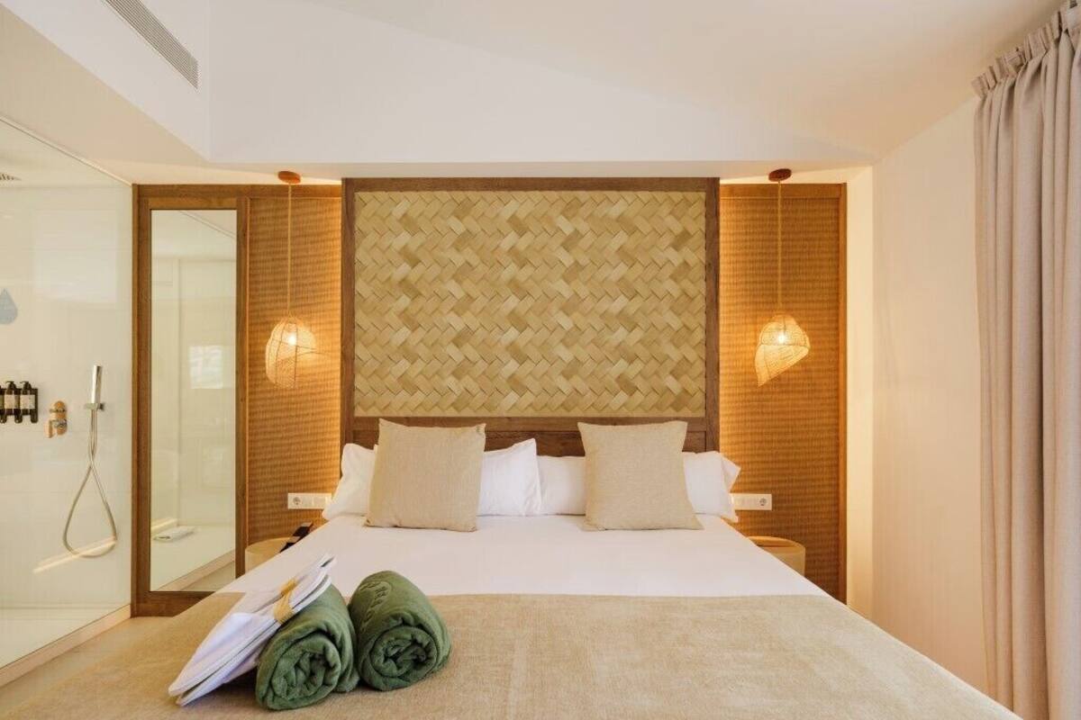 A hotel room with a bed, a shower, and a wall with a woven pattern.