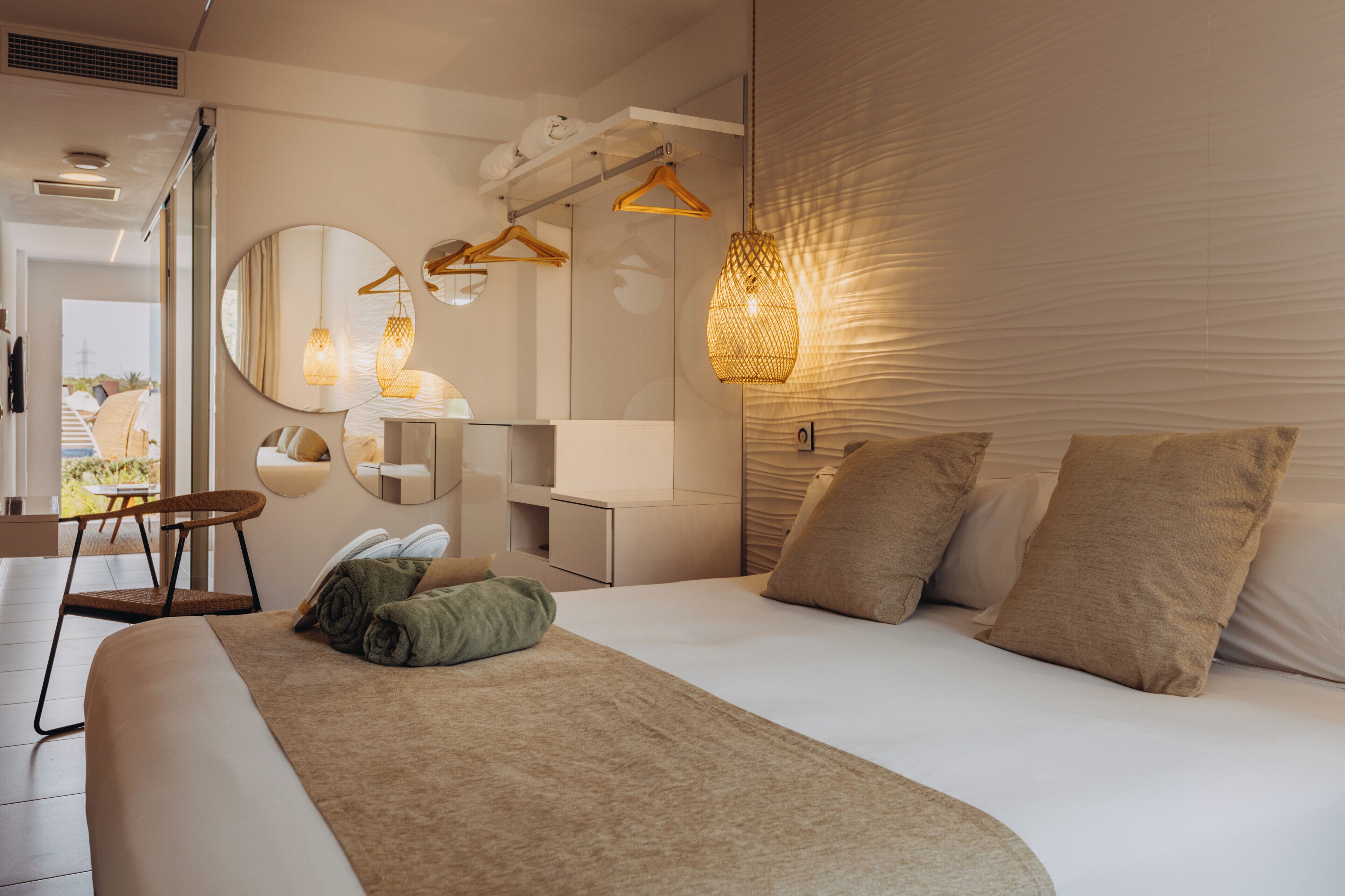 A modern hotel room with a bed, a chair, a mirror, and a hanging light fixture.