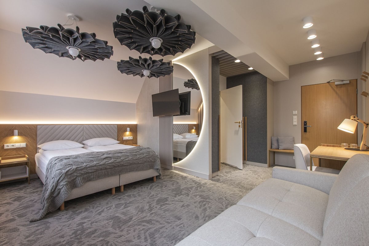 A modern hotel room with a large bed, a desk, a chair, and a TV.