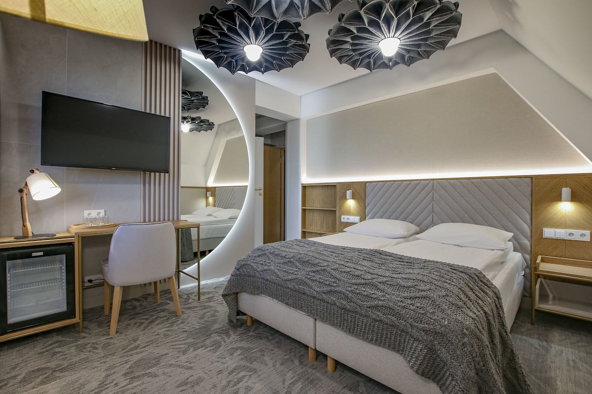 A modern hotel room with a bed, a desk with a computer, a chair, and a television.