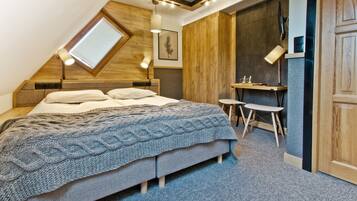 A bedroom with a sloped ceiling, a bed with a knitted blanket, a desk with two chairs, and a wooden wardrobe.