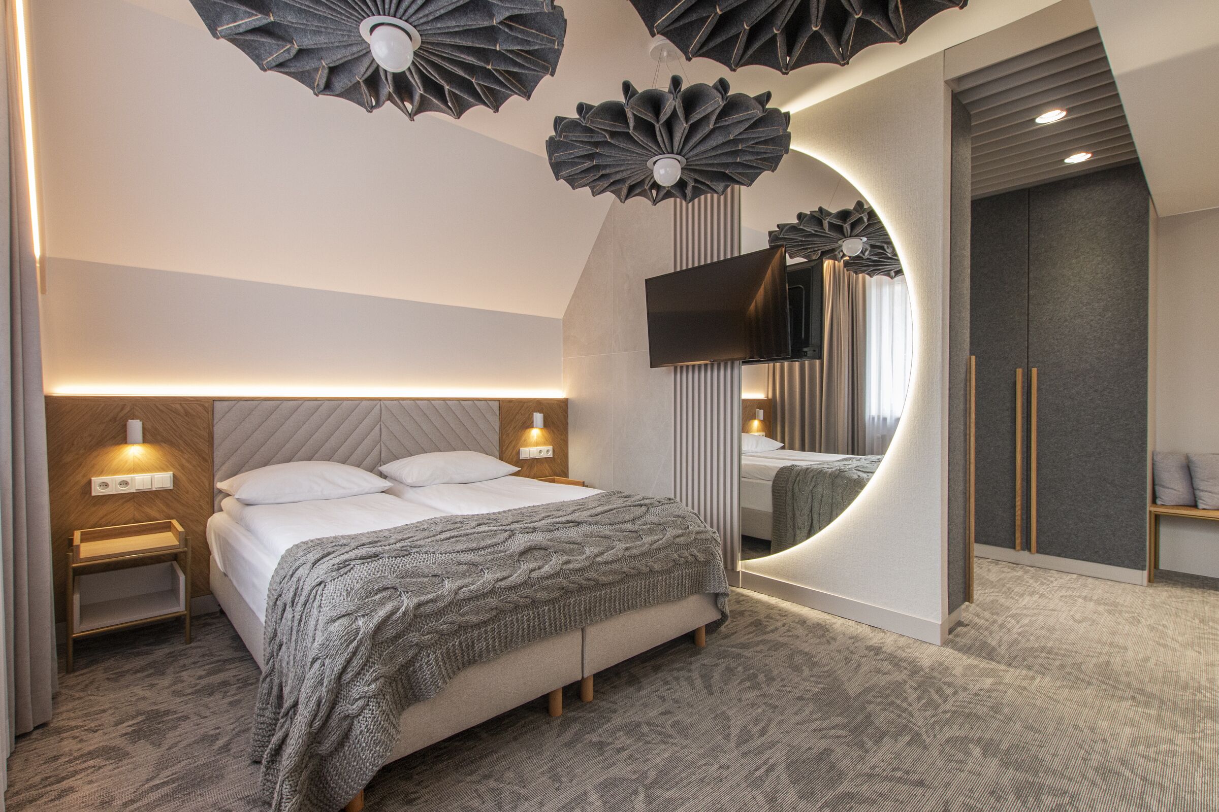 A modern hotel room with a large bed, a flat-screen TV, and unique ceiling light fixtures.