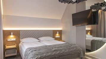 Een moderne slaapkamer met een groot bed, twee nachtkastjes met lampen, een flatscreen televisie en decoratieve plafondlampen.