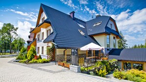 A modern two-story building with a sloped roof, a reception area with a sign, and a landscaped garden. - Pensjonat Tatry (Koscielisko)